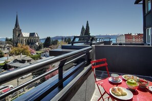 Un balcon avec une table préparée pour le petit-déjeuner, d’où l’on peut admirer une église et des montagnes.