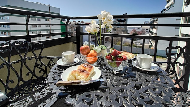 Un balcón con una mesa dispuesta para el desayuno, que incluye croissants, fresas y un jarrón con flores.