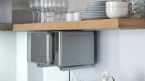 Una cocina con microondas integrado y repisa de madera con vasos y cuencos.