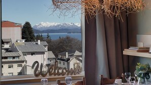 A dining table with a view of snow-capped mountains and a lake, a 'Welcome' sign, and a vase with flowers. - Montaña apartment with lake view and parking in Bariloche (San Carlos de Bariloche)