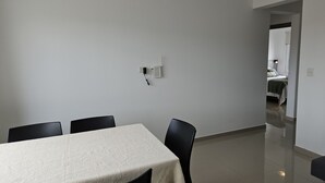 Un comedor con una mesa y sillas, un enchufe de pared, y una puerta que da a otra habitación.