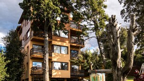 A multi-story building with balconies, surrounded by trees and a small garden area. - Namaste apartment with pool and recreational area in Bariloche (San Carlos de Bariloche)