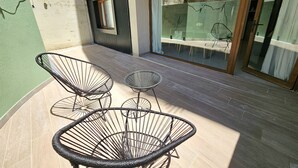 Eine Terrasse mit zwei schwarzen Gestellstühlen und einem kleinen runden Tisch.