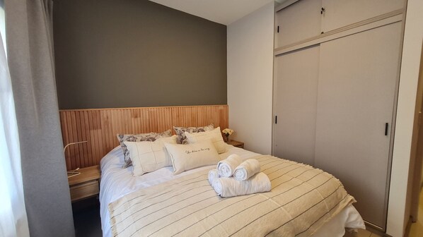 A neatly made bed with a striped blanket, pillows with floral patterns, and rolled towels on the bed.
