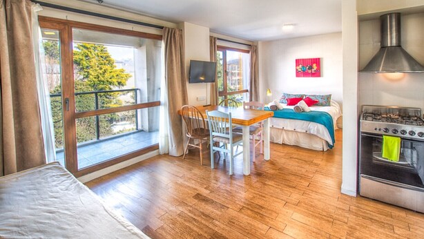 Een kamer met een bed, een eettafel met stoelen, een televisie en een keuken met een fornuis.