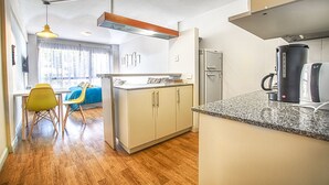 A compact kitchen with a refrigerator, coffee maker, and a dining area with chairs and a table.