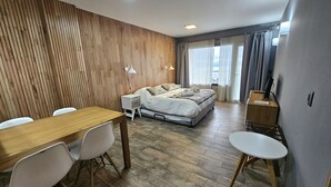 Une chambre d ’hôtel moderne avec un mur lambrissé en bois, un grand lit, une table à manger en bois avec des chaises et un petit bureau avec une chaise.