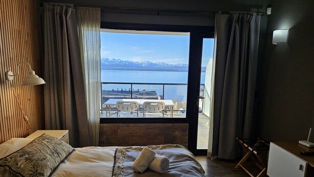 Une chambre d’hôtel avec un lit, un bureau, une lampe et une vue sur un plan d’eau et des montagnes.