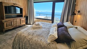 A bedroom with a large bed, a wooden dresser, a television, and a view of the sea. - Suizo II Romantic apartment with Nahuel Huapi Lake (San Carlos de Bariloche)
