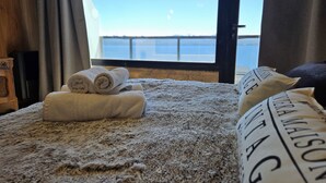 A bed with rolled towels, a window with a view of a body of water, and a pillow with text. - Suizo II Romantic apartment with Nahuel Huapi Lake (San Carlos de Bariloche)