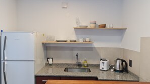 A compact kitchen with a refrigerator, a sink, a toaster, a kettle, and a shelf with dishes and glasses. - Swiss IV apartment with an impressive lake view Nahuel Huapi (San Carlos de Bariloche)