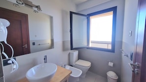 A bathroom with a large mirror, a sink, a bidet, a toilet, and a window. - Swiss IV apartment with an impressive lake view Nahuel Huapi (San Carlos de Bariloche)