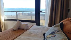 A hotel room with a bed, a window with a view of mountains and a body of water, and a balcony with a railing. - Swiss IV apartment with an impressive lake view Nahuel Huapi (San Carlos de Bariloche)