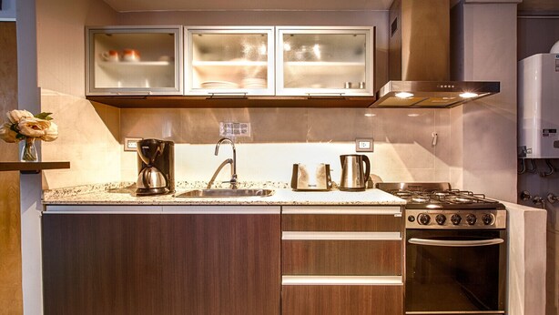 A compact kitchen with a built-in stove, oven, and sink, wooden cabinets, and a small countertop.