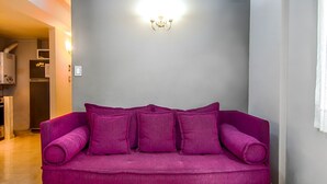A purple sofa with multiple cushions in a room with a grey wall and a light fixture above it.