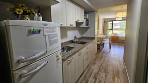 Eine kompakte Küche mit Kühlschrank, Mikrowelle und einer Arbeitsplatte aus Granit. Durch einen offenen Durchgang ist ein Essbereich mit Tisch und Stühlen zu sehen.
