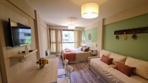 Ein Hotelzimmer mit Bett, Sofa, Fernseher, Tisch mit Blumenvase und grüner Wand mit Kleiderhaken.