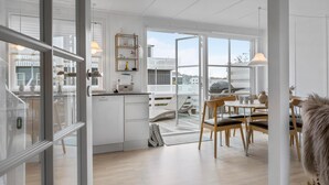 Una cocina moderna con armarios blancos, horno integrado y un comedor con sillas y mesa de madera.