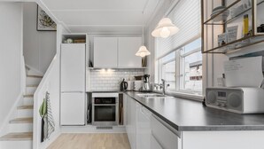 Una cocina moderna con armarios blancos, horno empotrado, microondas y cafetera. Hay una ventana con vistas a edificios.
