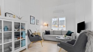 Una sala de estar moderna con un sofá gris, dos sillones, un aparador de vidrio y un televisor montado en la pared.