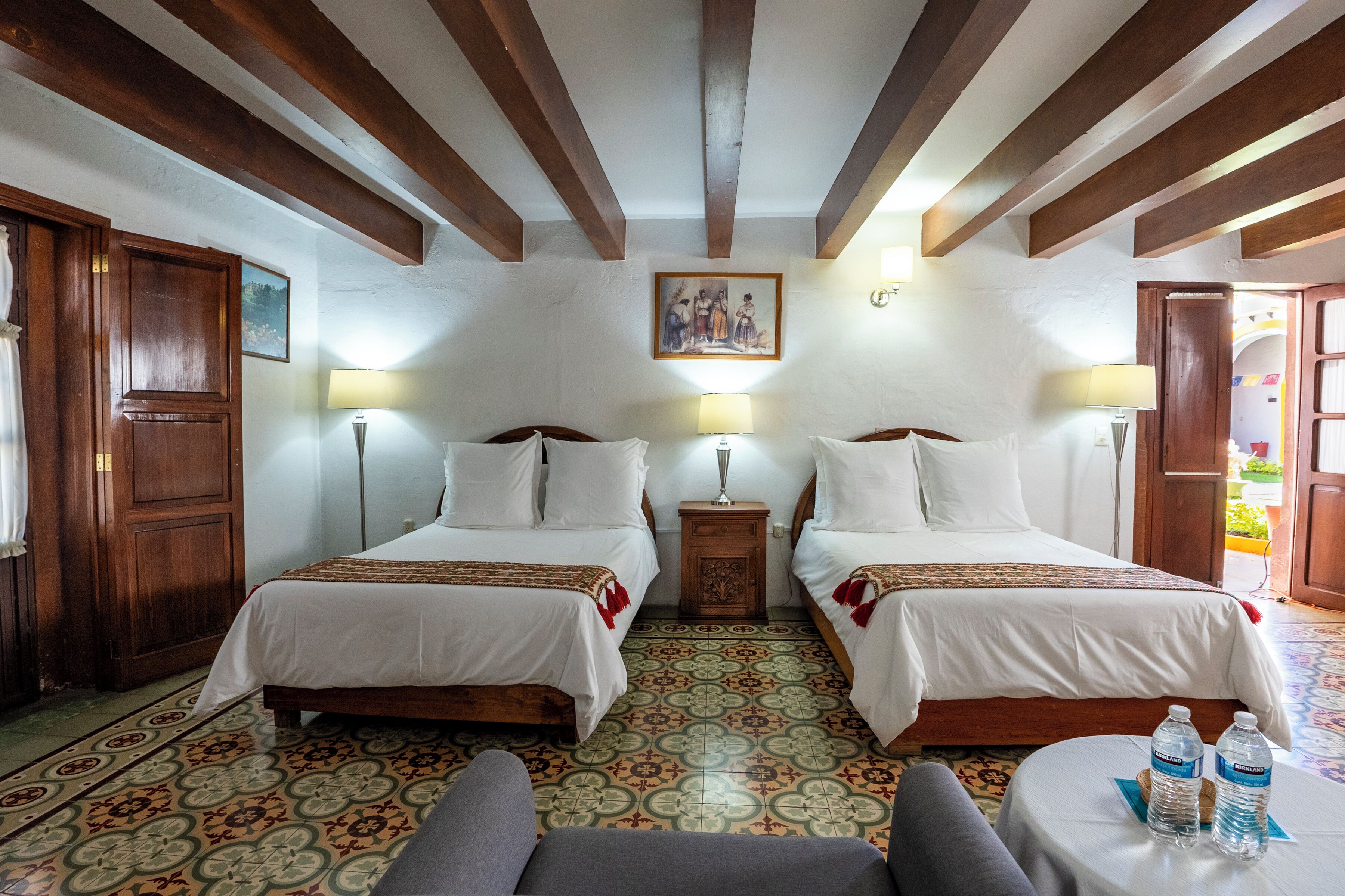 A room with two beds, a small table with water bottles, and a patterned floor.