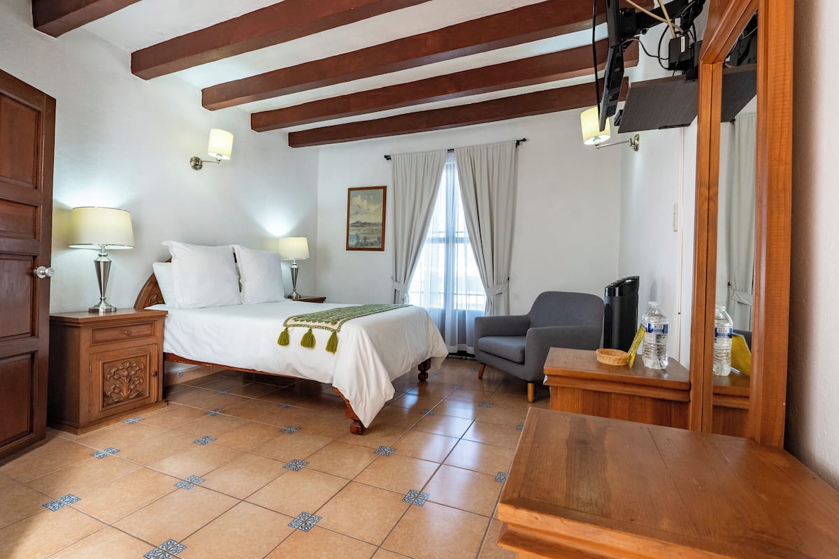 A bedroom with a bed, bedside lamps, a chair, a desk, and a window with curtains.