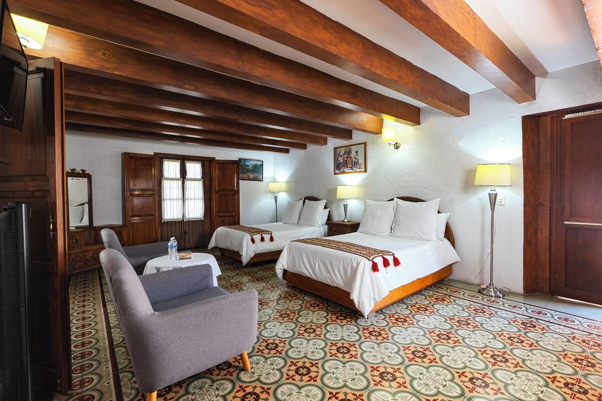 A hotel room with two beds, a sofa, a TV, and a patterned floor.