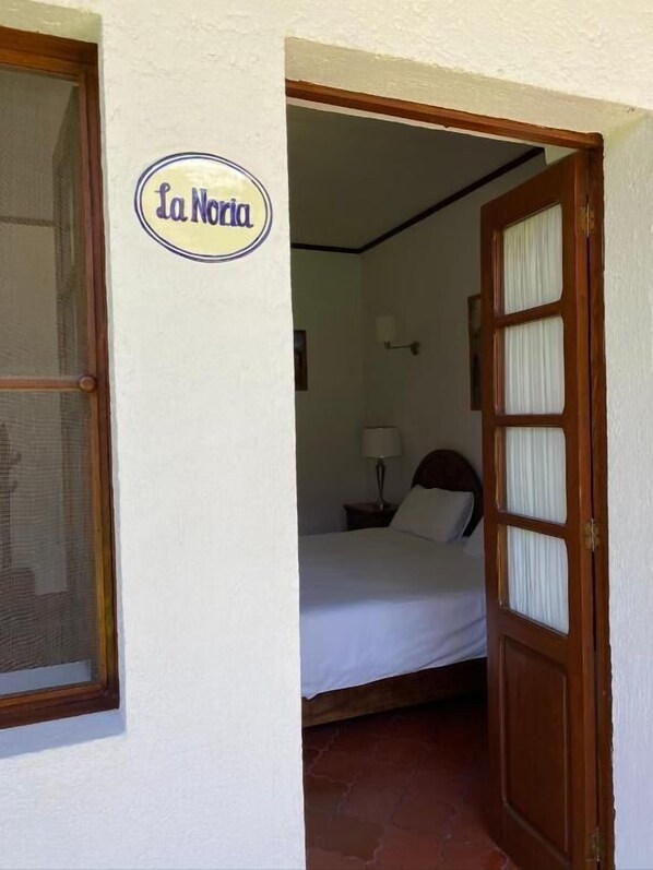 Um quarto com cama, mesa de cabeceira, luminária e porta com a placa 'La Noria'.