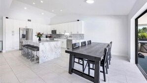 A modern kitchen with white cabinets, a marble island, and a dining area with a dark wooden table and chairs.
