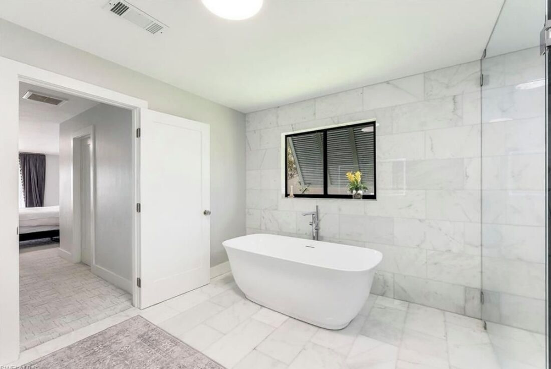 A modern bathroom with a freestanding bathtub, a glass shower enclosure, and a small window with blinds.