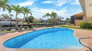 A swimming pool with a clear blue water, surrounded by palm trees and a brick pathway.
