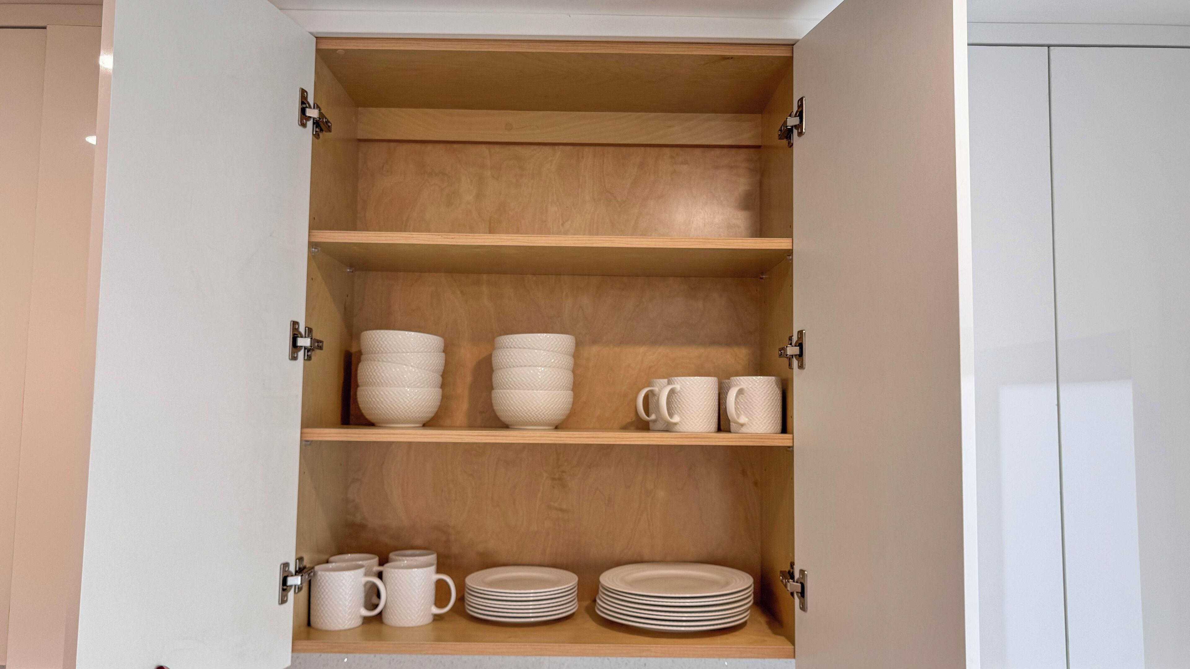 A wooden cabinet with three shelves, each holding bowls, mugs, and plates.