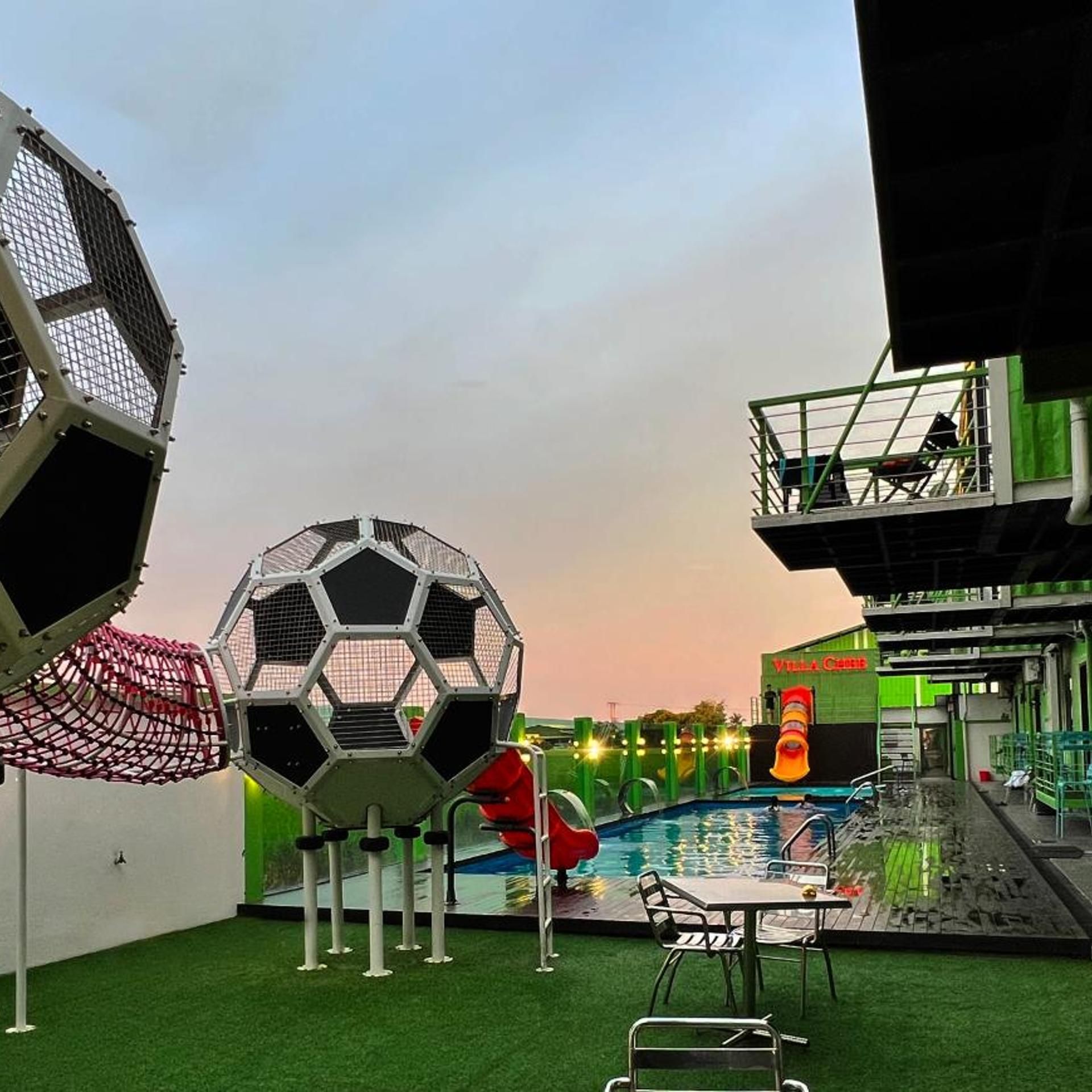 A pool area with artificial grass, a soccer ball sculpture, and a building with a green facade.