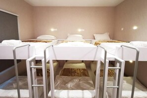 Een hotelkamer met drie eenpersoonsbedden, elk met een witte matras en een gouden accent.