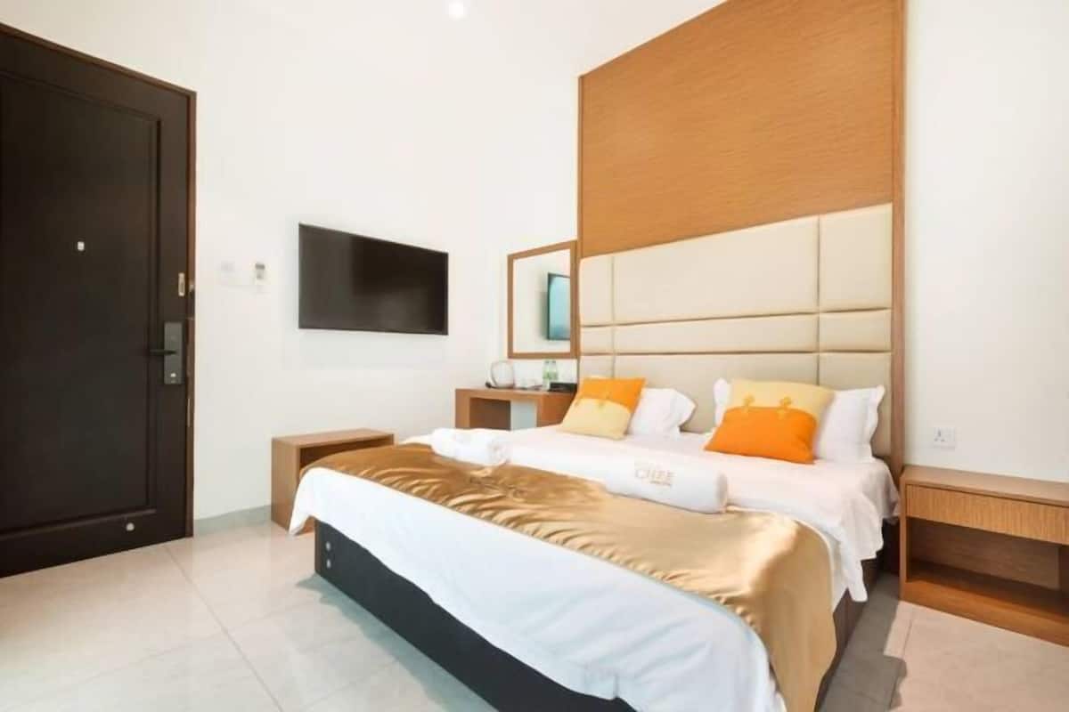 A hotel room with a large bed, a TV mounted on the wall, and a wooden headboard.