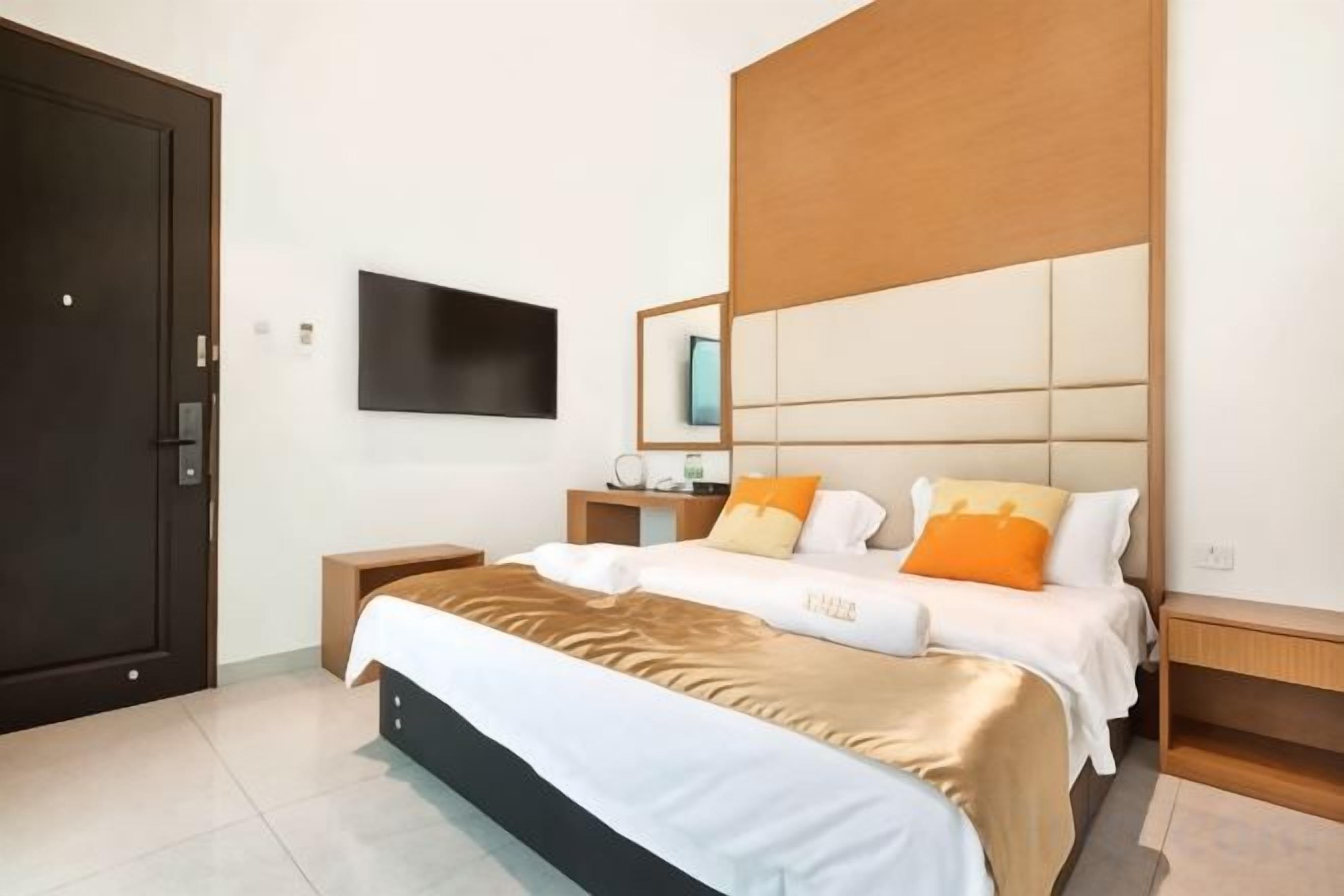 A hotel room with a large bed, a flat-screen TV mounted on the wall, a wooden headboard, and a wooden nightstand.
