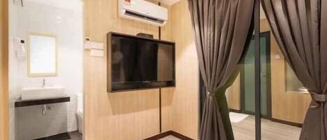 A hotel room with a flat-screen TV mounted on the wall, a sink, and a large window with curtains.