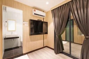 A hotel room with a flat-screen TV mounted on the wall, a sink, and a large window with curtains.