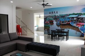 A living room with a sofa, ottoman, and a dining area with chairs. A staircase is visible in the background. - Villa Chee (Sekinchan)