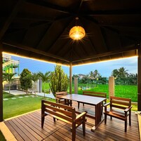 Un espacio de estar al aire libre techado, con mobiliario de madera y una lámpara colgante.