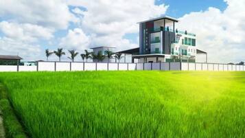 A modern building with a flat roof, surrounded by a white fence, and a lush green field in the foreground.