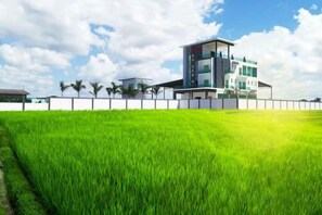 A modern building with a flat roof, surrounded by a white fence, and a lush green field in the foreground. - Villa Chee (Sekinchan)