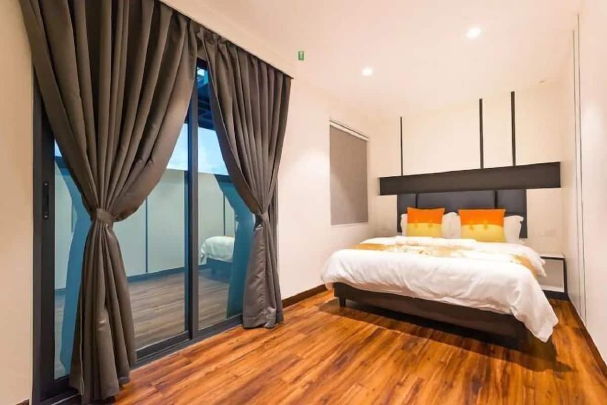 A modern hotel room with a large bed, dark curtains, and a wooden floor.
