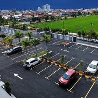 Ein Parkplatz mit mehreren Autos, Palmen und einem Blick auf eine Stadtlandschaft im Hintergrund.