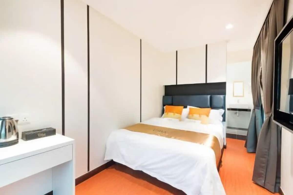 A hotel room with a bed, a bedside table, a TV, and a window.