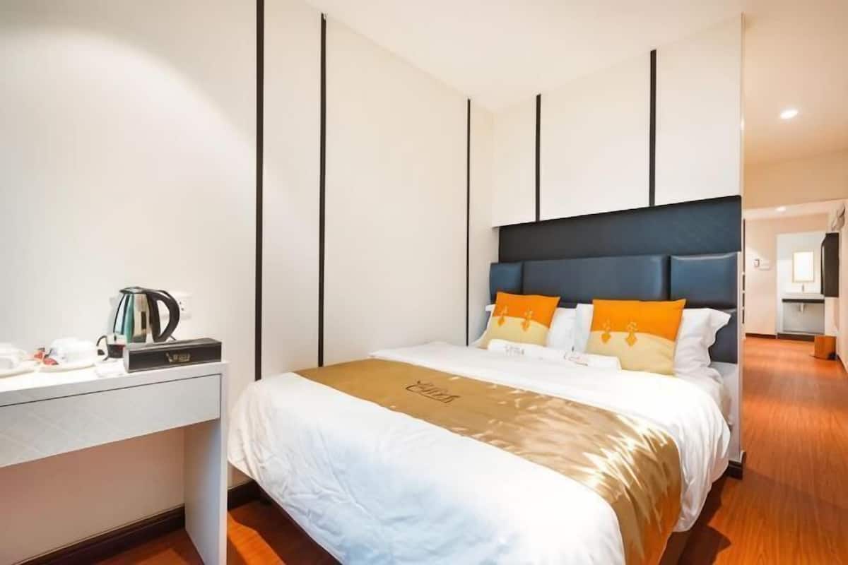 A hotel room with a bed, bedside table, and a desk with a kettle.