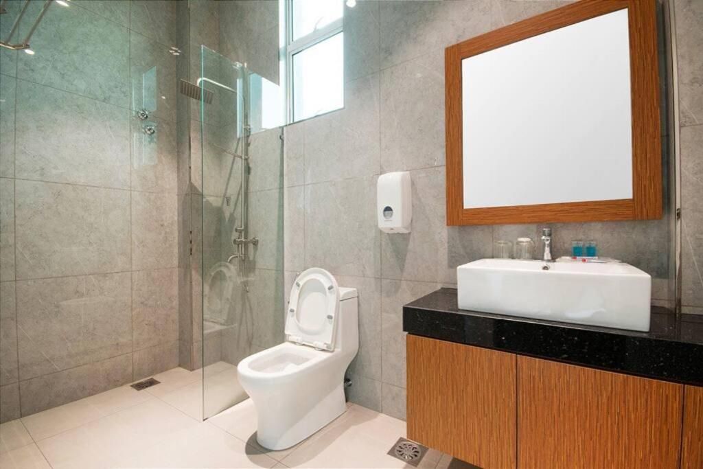A modern bathroom with a glass-enclosed shower, a white toilet, a wooden cabinet, and a large mirror.