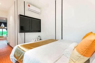 A hotel room with a bed, a flat-screen TV mounted on the wall, and an air conditioning unit.