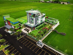 A modern building with a flat roof, surrounded by green fields and a parking lot. - Villa Chee (Sekinchan)