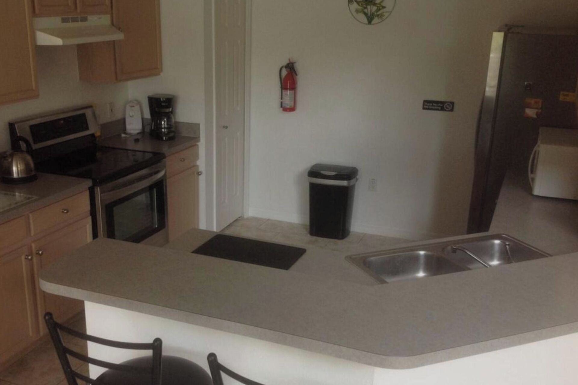 A kitchen with a central island, a coffee maker, a fire extinguisher, and a trash bin.